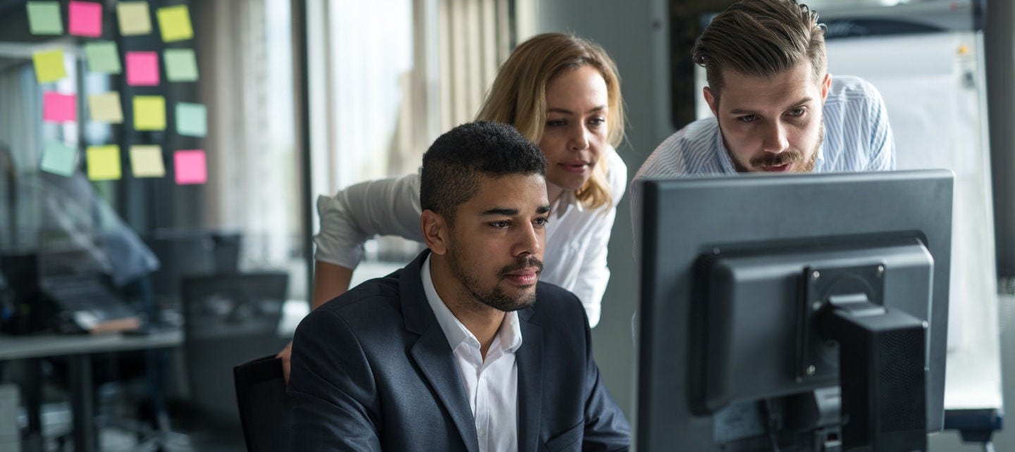 Three employees look at a computer with concern. 