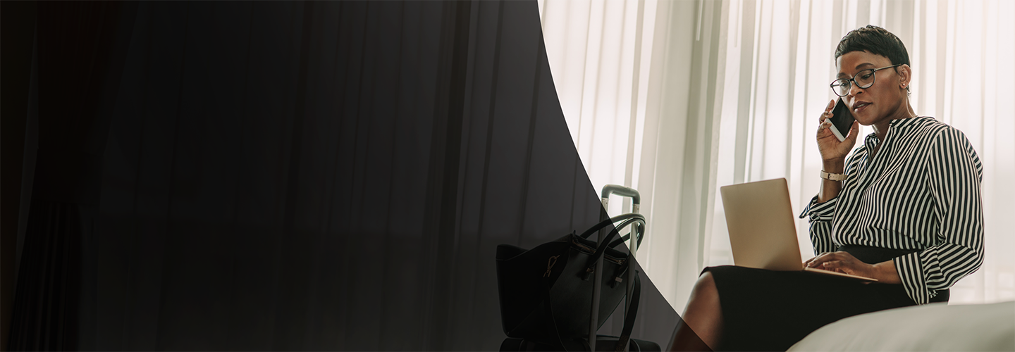 Woman on phone looking at her laptop in hotel