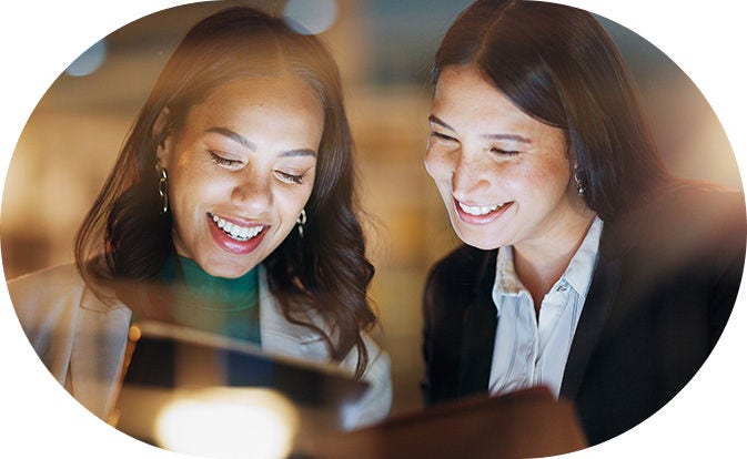 Deux femmes souriantes regardant un écran, illustrant la collaboration dans un environnement de travail positif.
