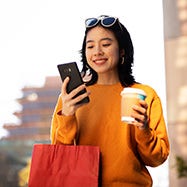 joven asiática feliz con teléfono y café en sus manos.