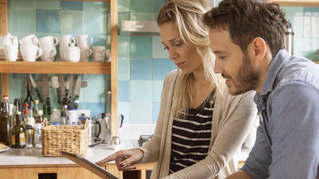 Two people look at a tablet in a kitchen. 