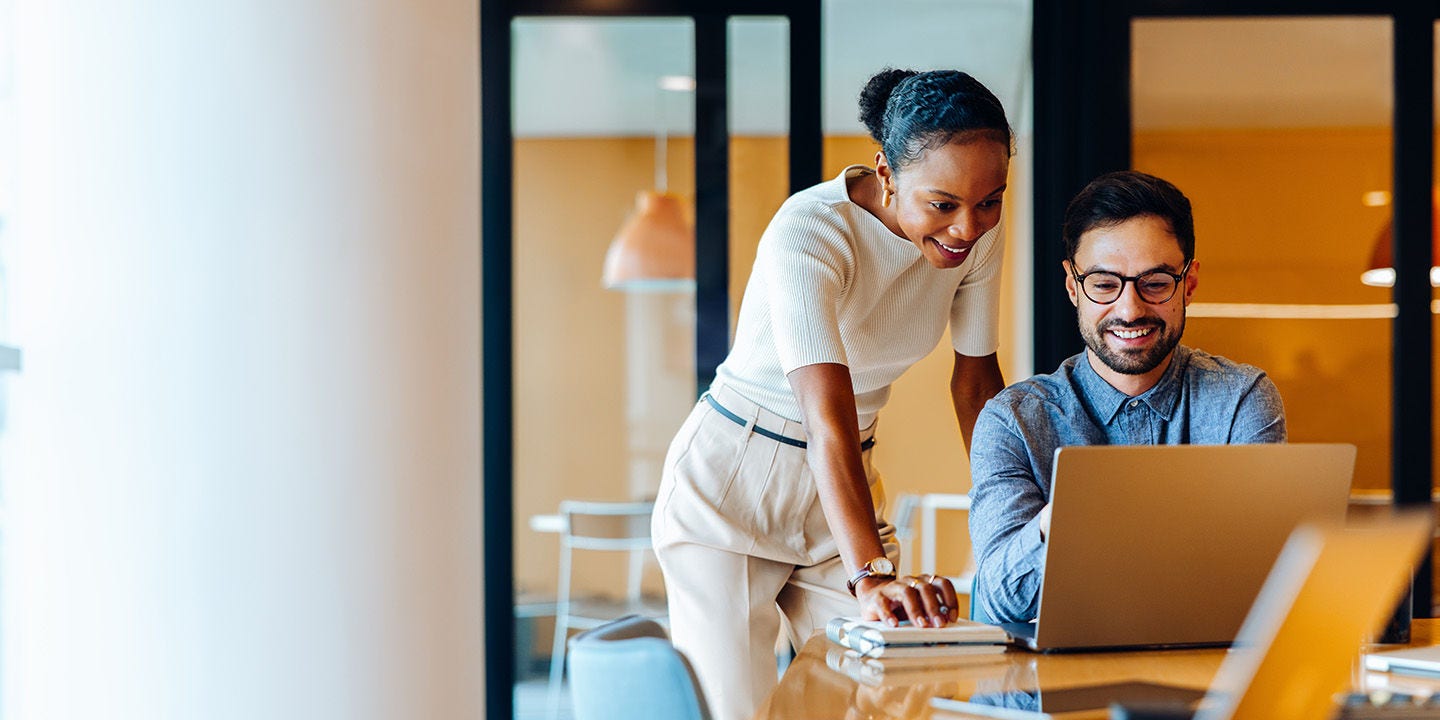 Two coworkers smiling while using a work laptop