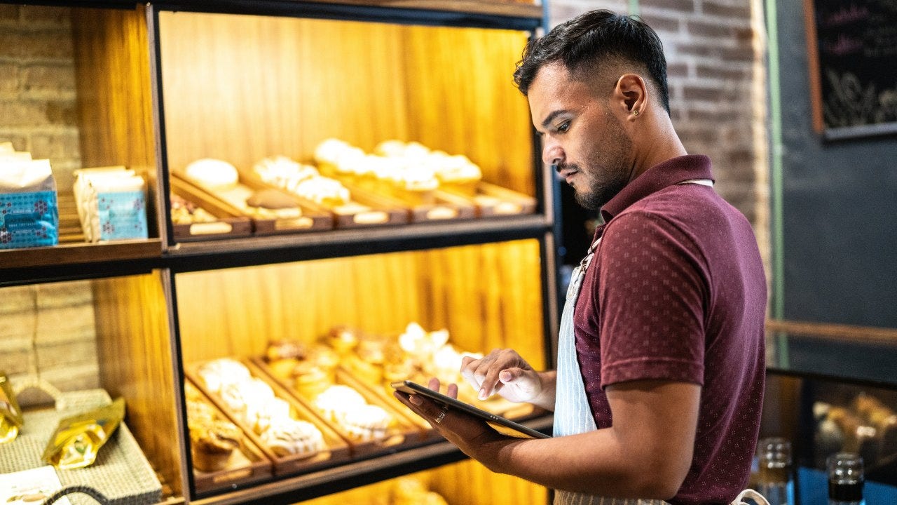 Un hombre mira una tableta frente a una exhibición de productos horneados. 
