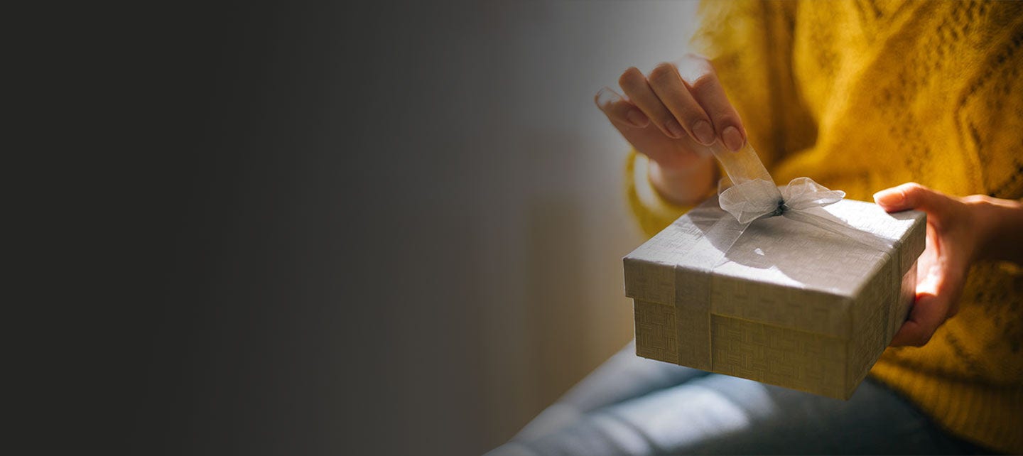 Person unwrapping a bow on a wrapped gift box containing a Mastercard gift card.