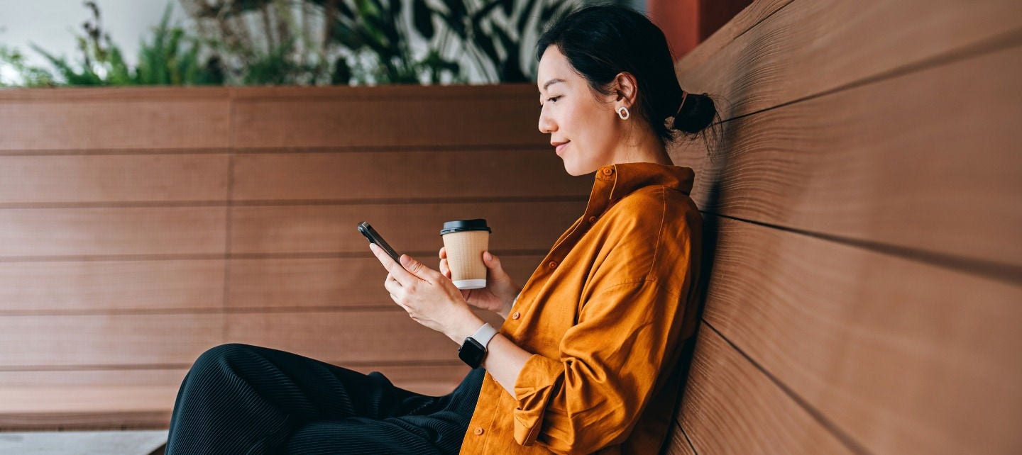A woman sits on a bench and smiles at her phone. 