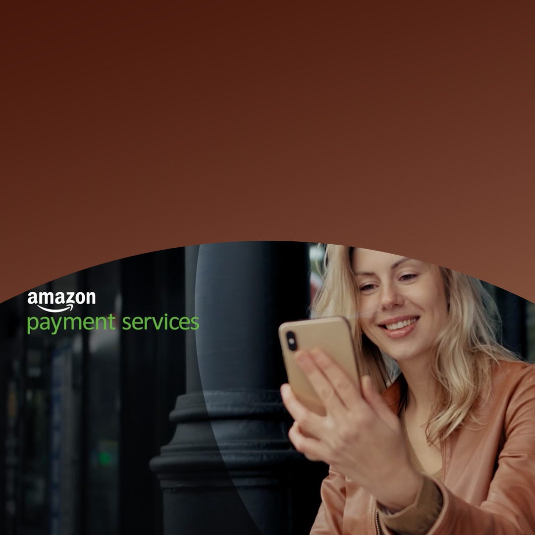 Woman in a brown jacket smiling at her smartphone, using amazon payment services with mastercard gateway.