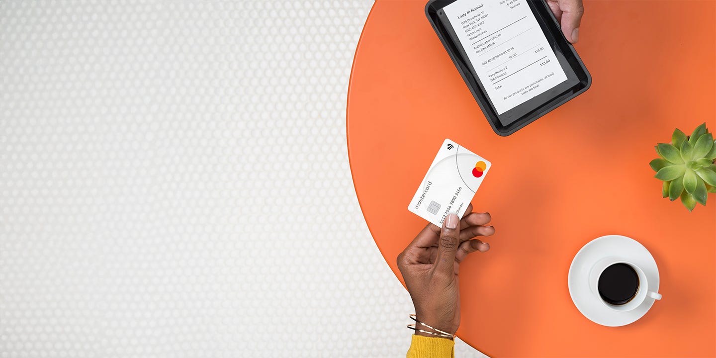 Клиент оплачивает покупку с помощью криптовалютной карты Mastercard, в то время как другая рука держит планшет с экраном оплаты.