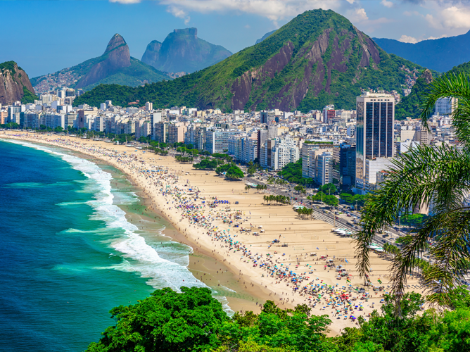 Vue panoramique de la plage de Copacabana à Rio de Janeiro, au Brésil, présentant un paysage urbain dynamique, un océan d’un bleu limpide et des montagnes verdoyantes en arrière-plan par une journée ensoleillée.