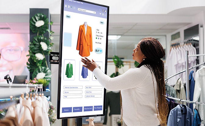 Une acheteuse choisit des vêtements sur un tableau numérique à écran tactile.