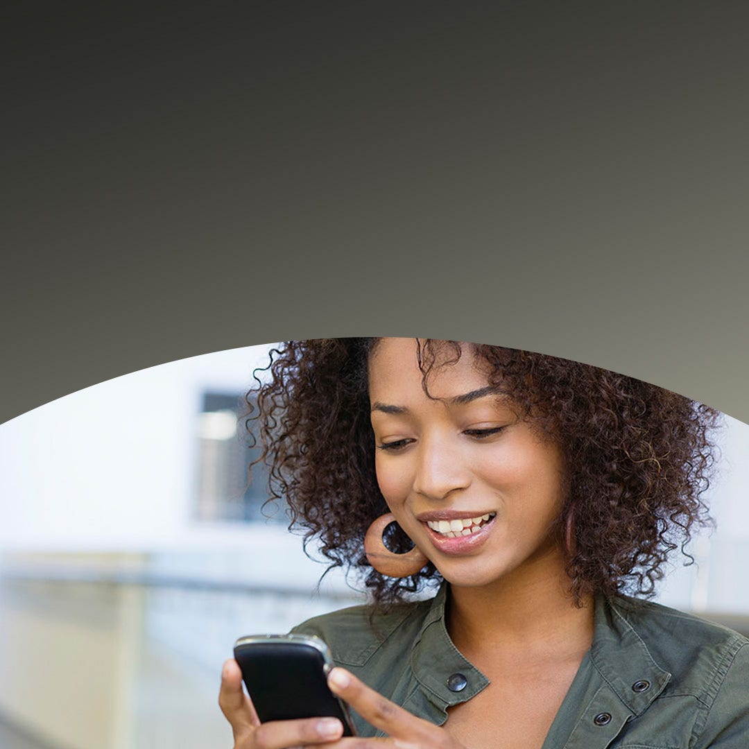A woman smiling while looking at her smartphone.