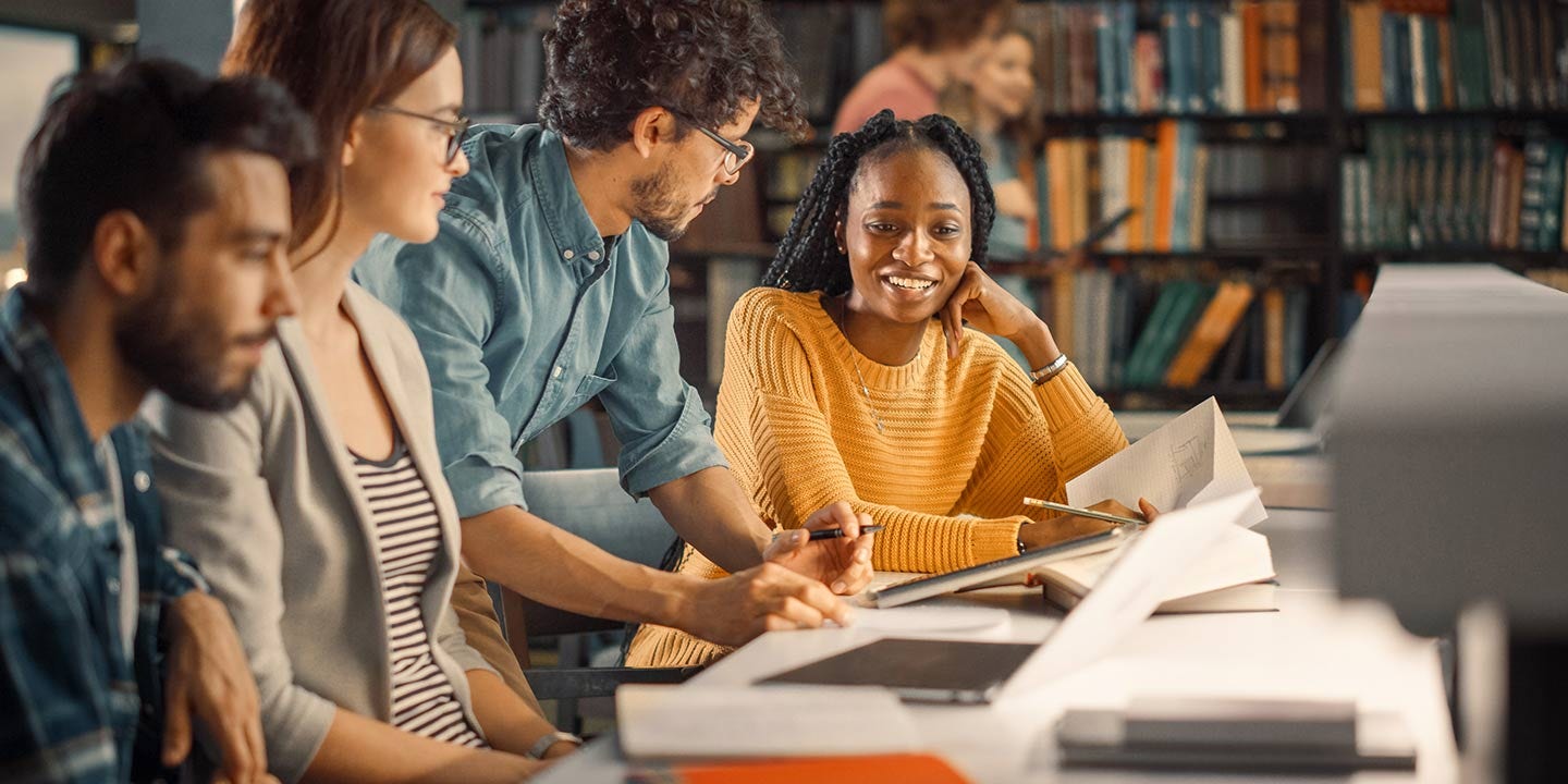 University library: Diverse group of gifted students have siscussion, use laptop, prepare for exams together, helping, researching subjects for paper sssignment. Happy young people study for future