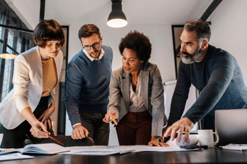 Grupo de personas de pie alrededor de una mesa trabajando en colaboración. 