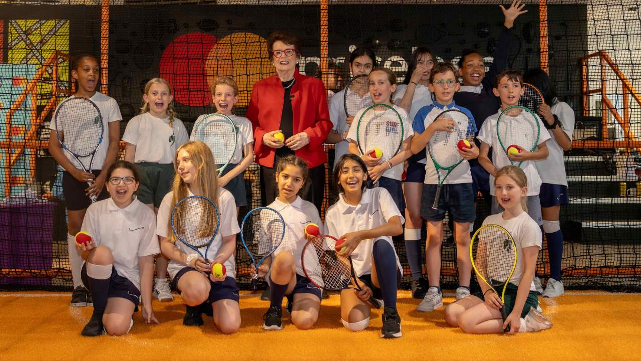 Bille Jean King stands with young tennis students holding their rackets . 