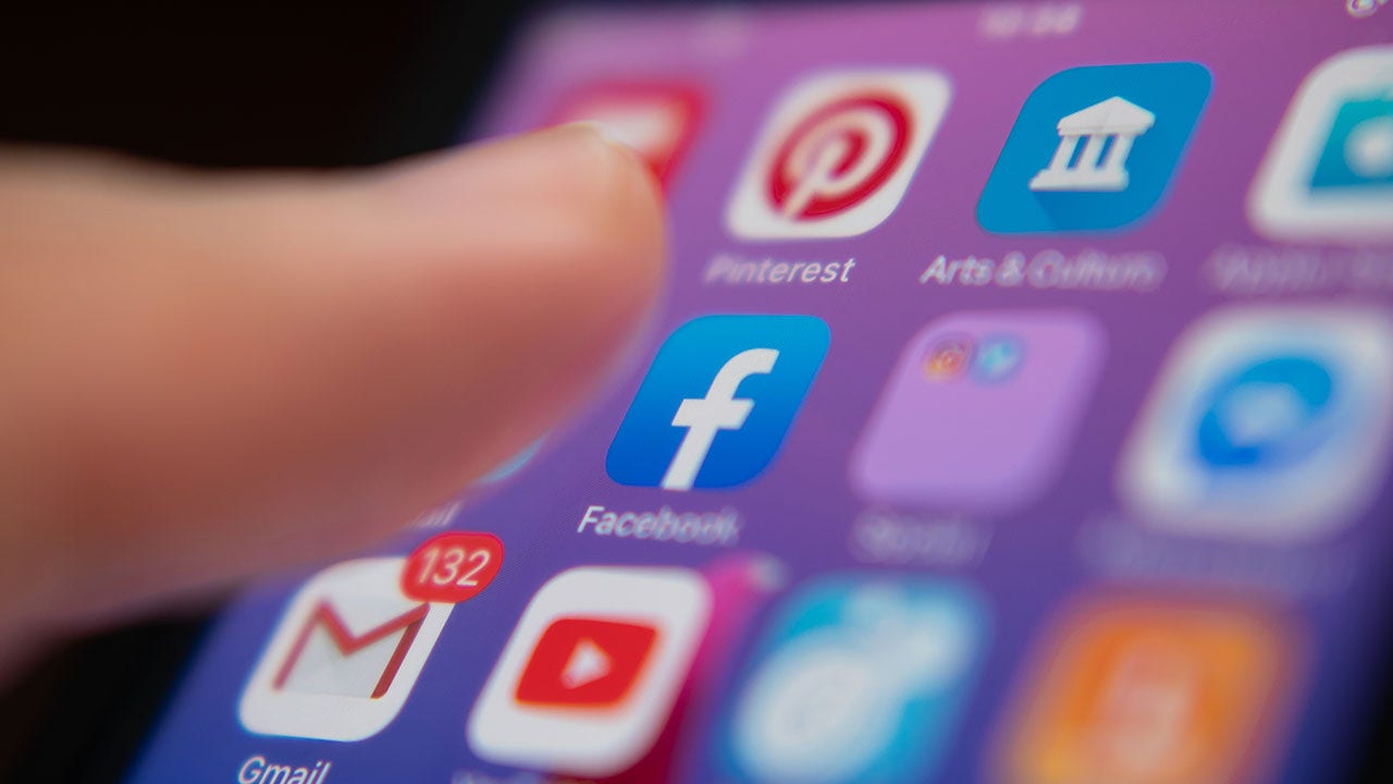 Usuario tocando el logotipo de Facebook en la pantalla de un teléfono.