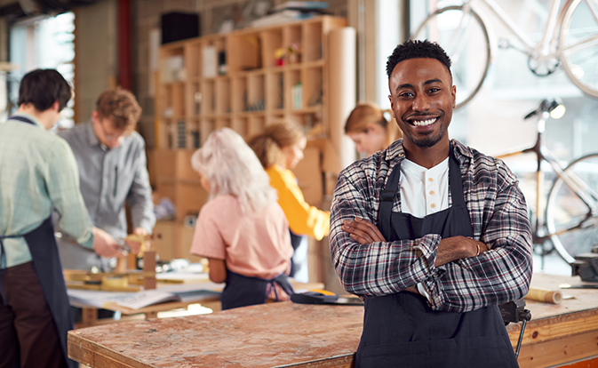 Un homme souriant à la caméra, se tenant au milieu d’un atelier de team building