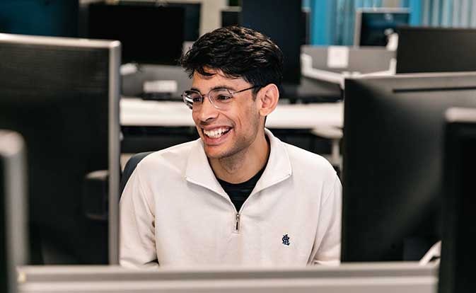 Smiling man in glasses sitting at a computer workstation.