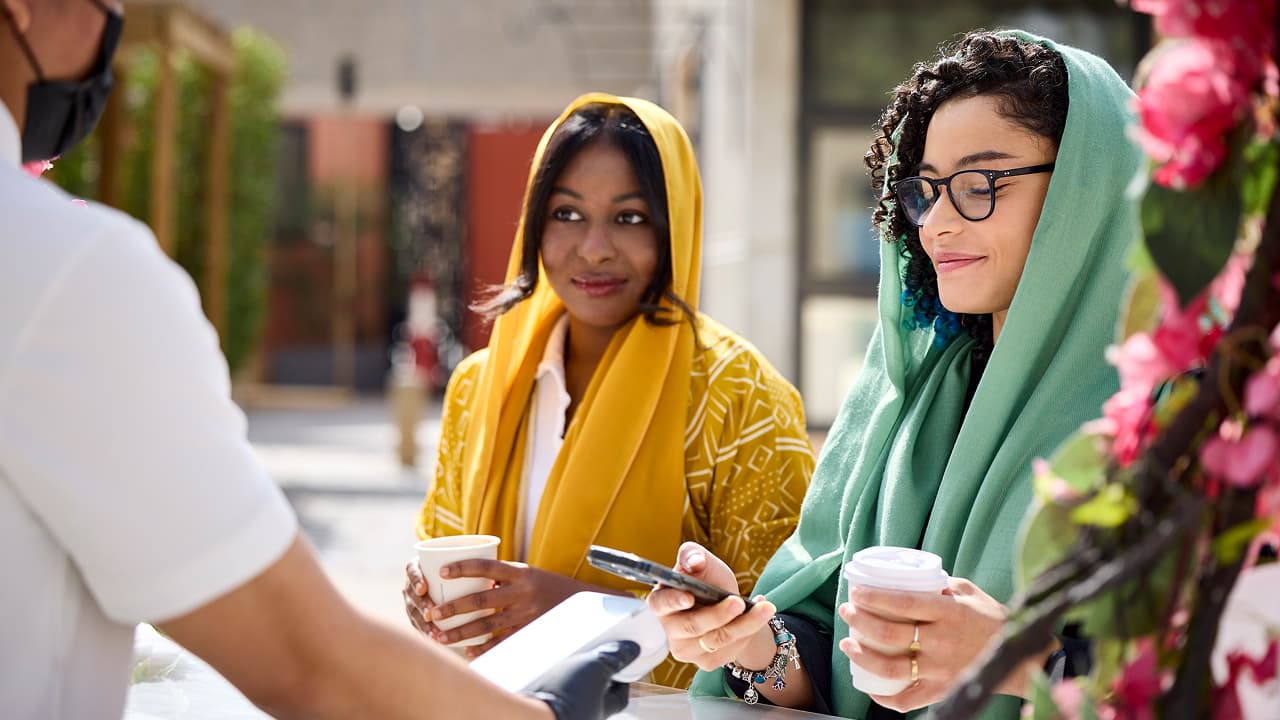امرأتان ترتديان الحجاب تشتريان القهوة باستخدام الدفع عبر الهاتف المحمول.