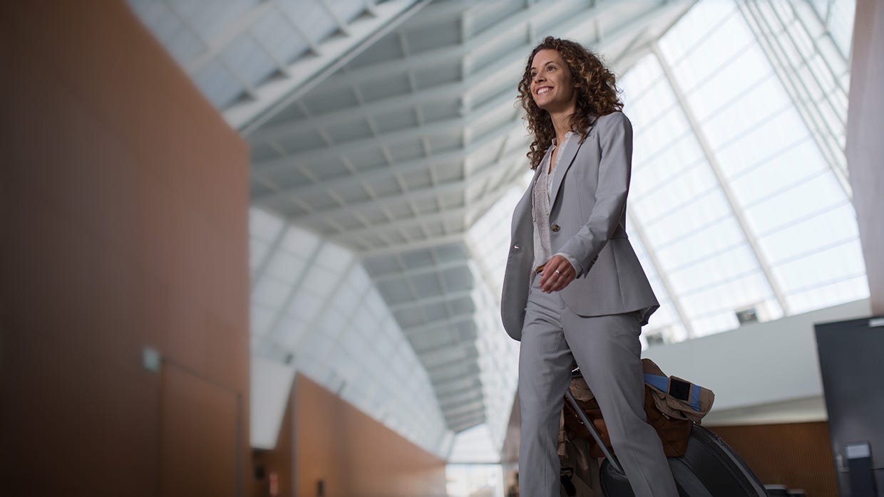 smiling businesswoman pulling luggage in airport.