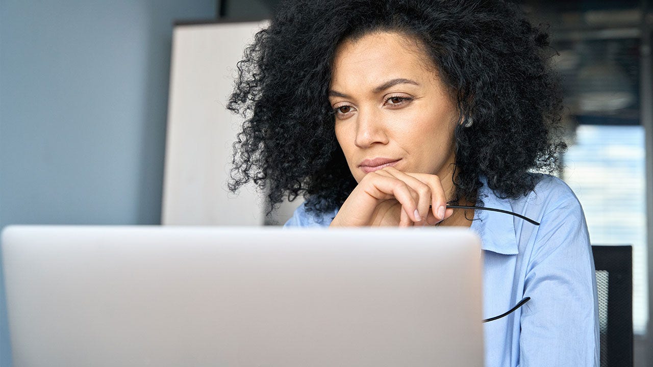 Mujer de negocios seria sentada en un escritorio, mirando una computadora portátil.