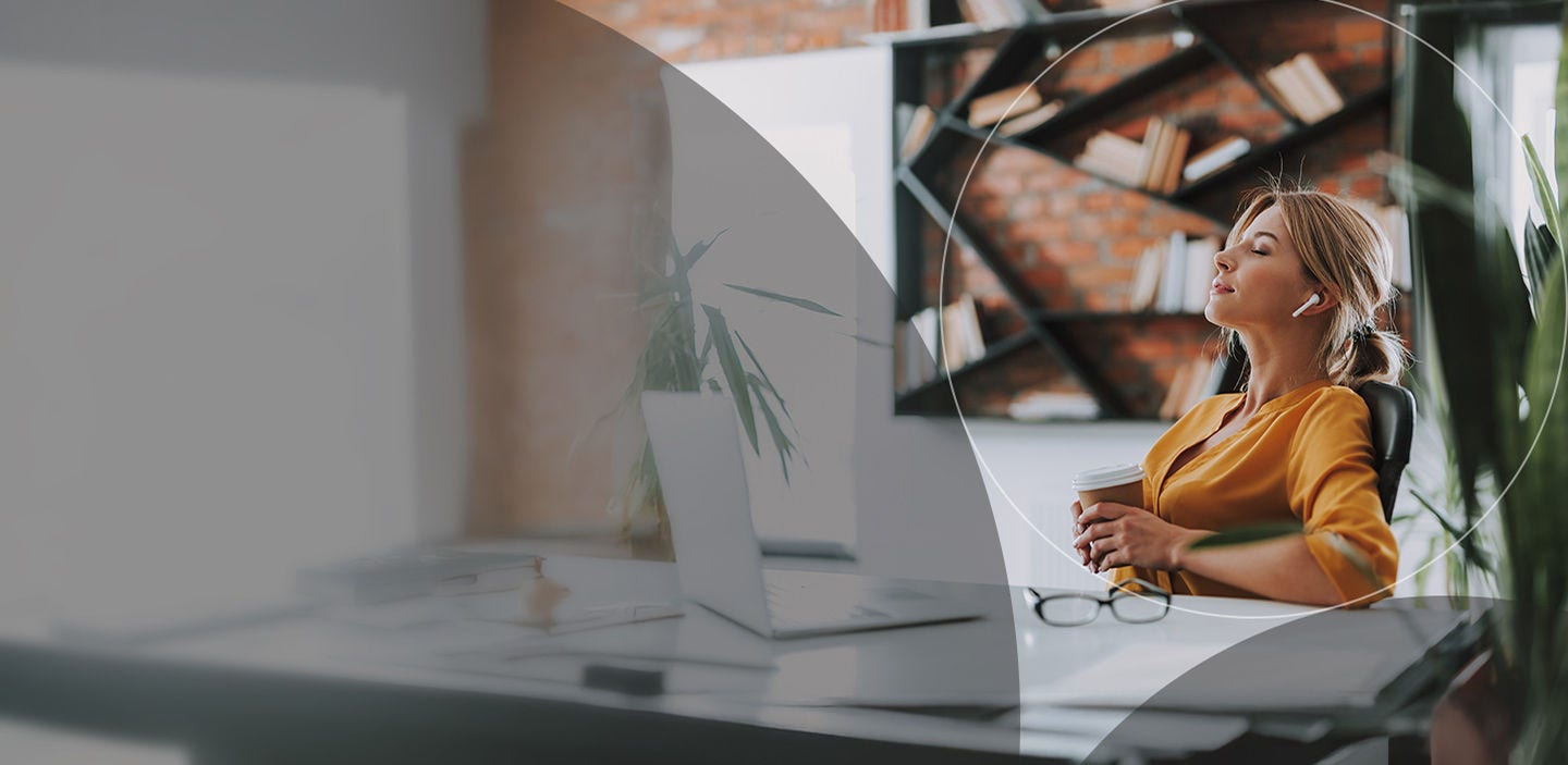 Femme se relaxant à son bureau, les yeux fermés, profitant d'un moment de tranquillité.