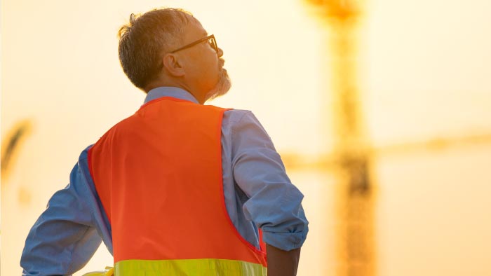 Construction worker looking into orange sky.