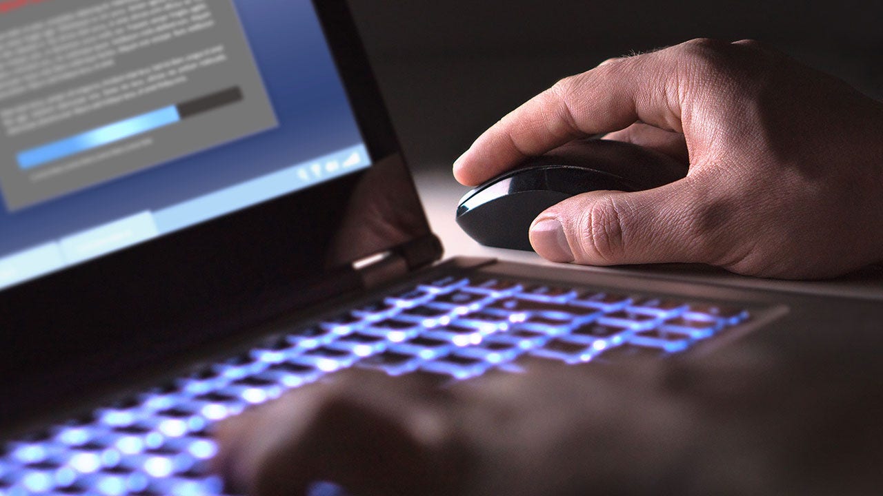 Hacker cargando programa ilegal en una habitación oscura.