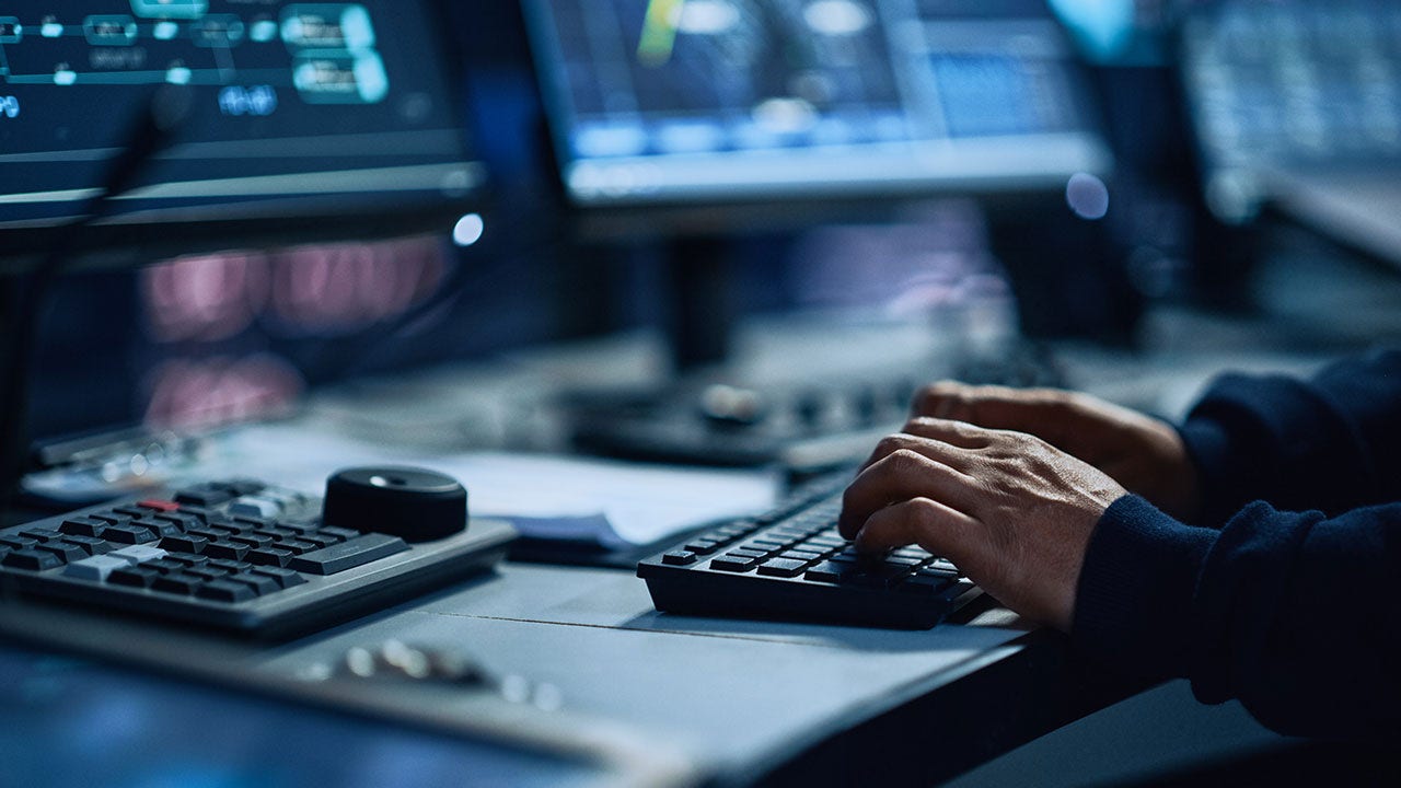 Spécialiste travaillant sur un ordinateur dans une salle de contrôle technologique équipée d’écrans numériques.