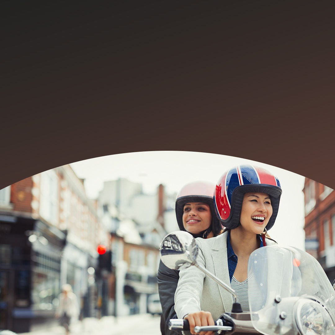 Dos mujeres circulando en scooter por la calle.