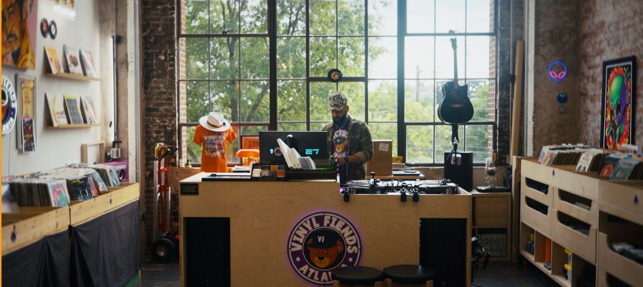 DJ Silver Knights looks at his computer among his record collection in front of a large window. 