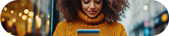 Une femme aux cheveux bouclés regarde son téléphone, concentrée sur l’écran. 