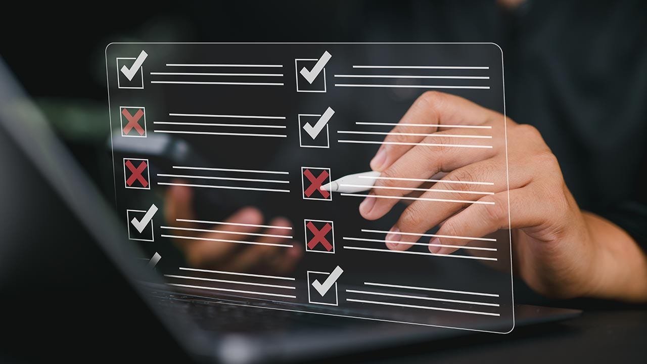 Des mains cochant une liste superposée devant un ordinateur portable.