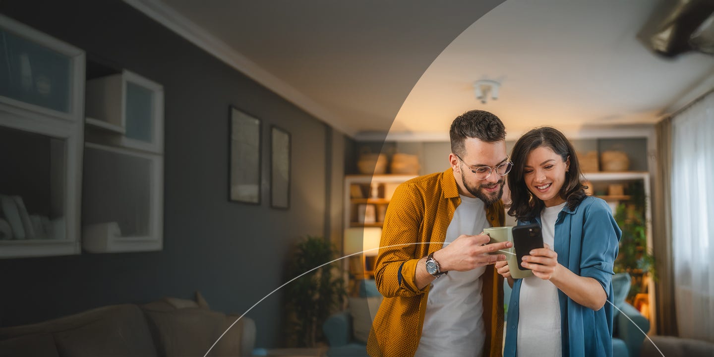 Esposo y esposa felices tomando una taza de café mientras usan el teléfono móvil.