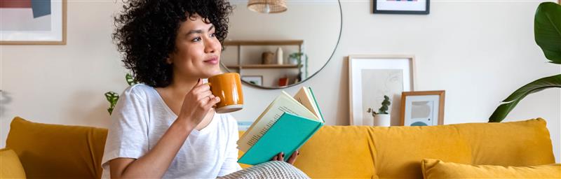 Femme assise sur un canapé avec une tasse de café, lisant un livre