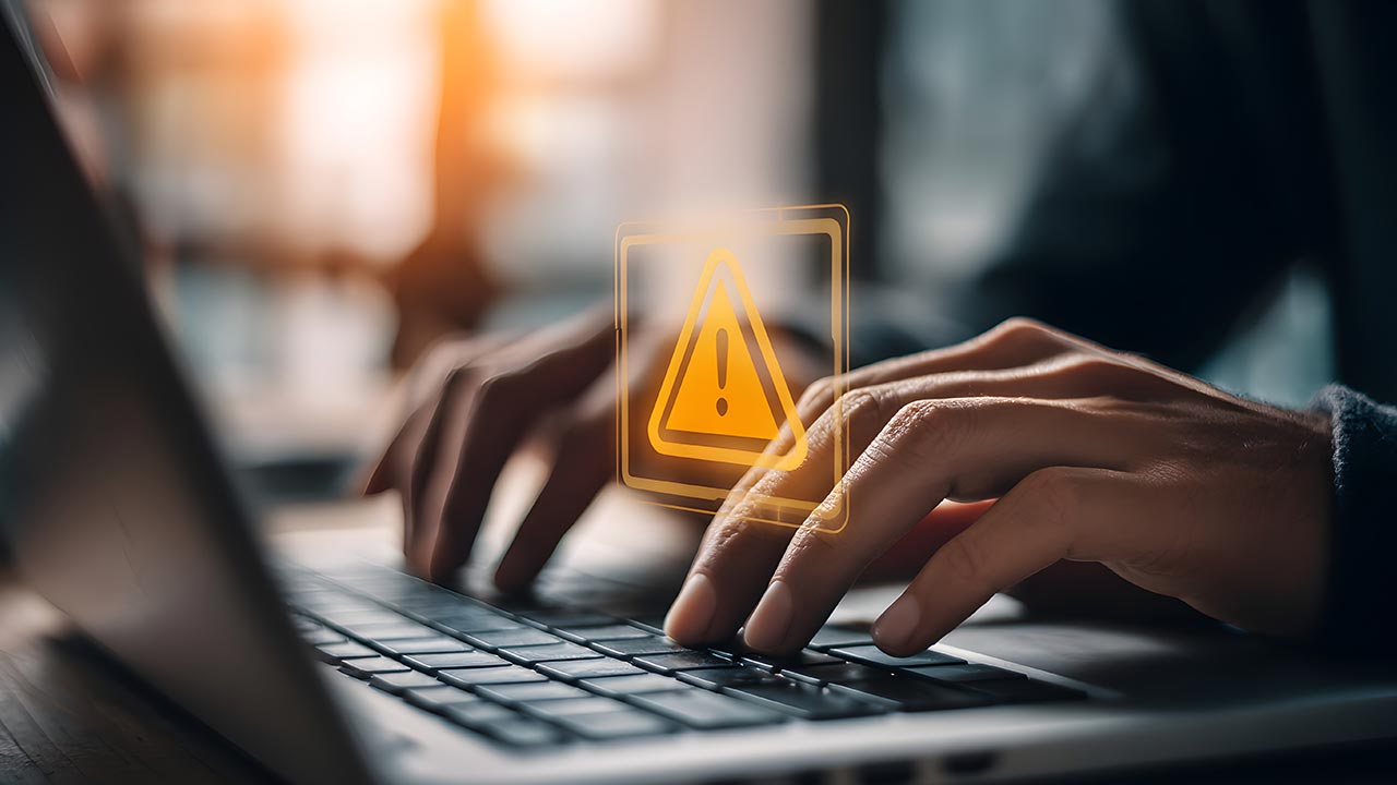 Primer plano de manos escribiendo en una computadora portátil con superposición de alerta de seguridad.