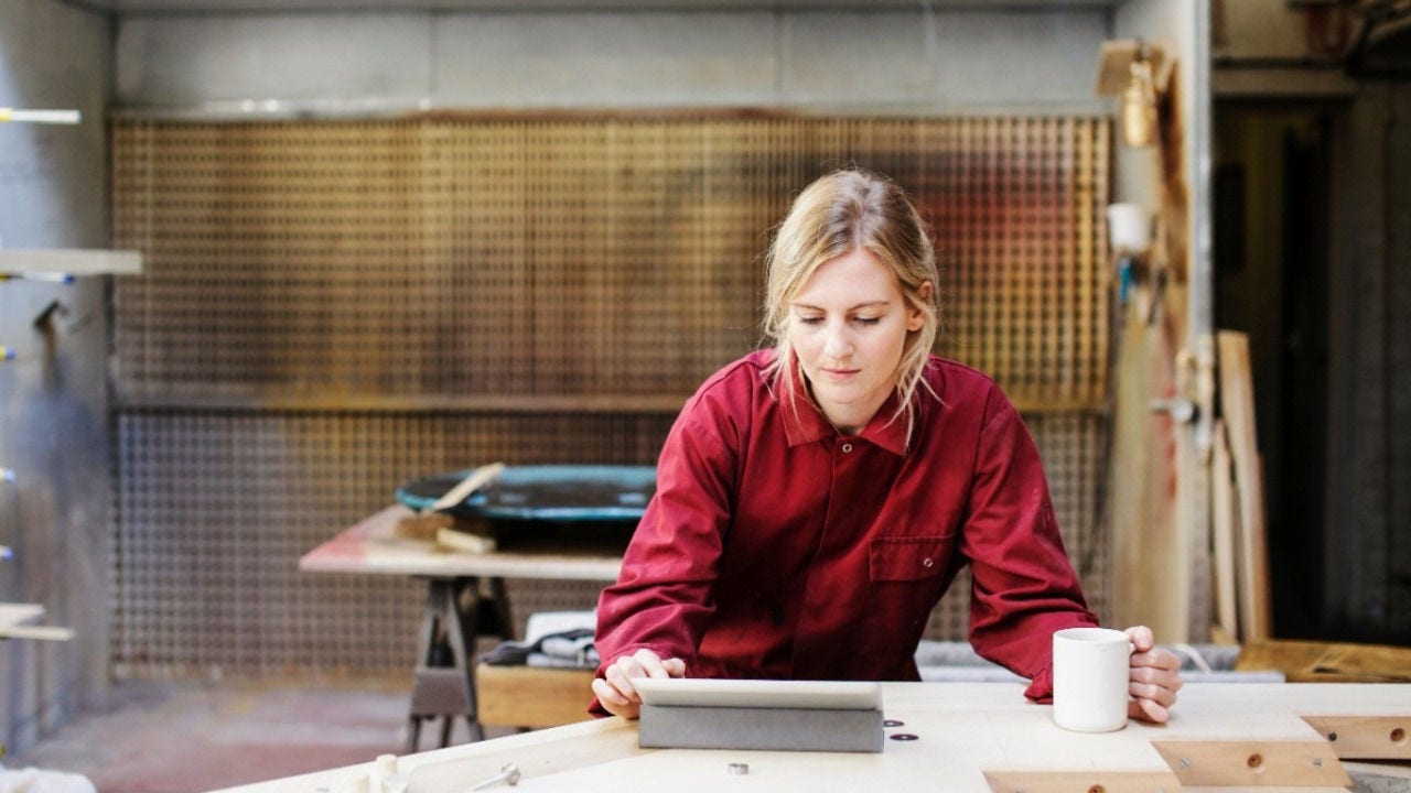 A small business owner looks at a digital pad while holding a cup of coffee. 