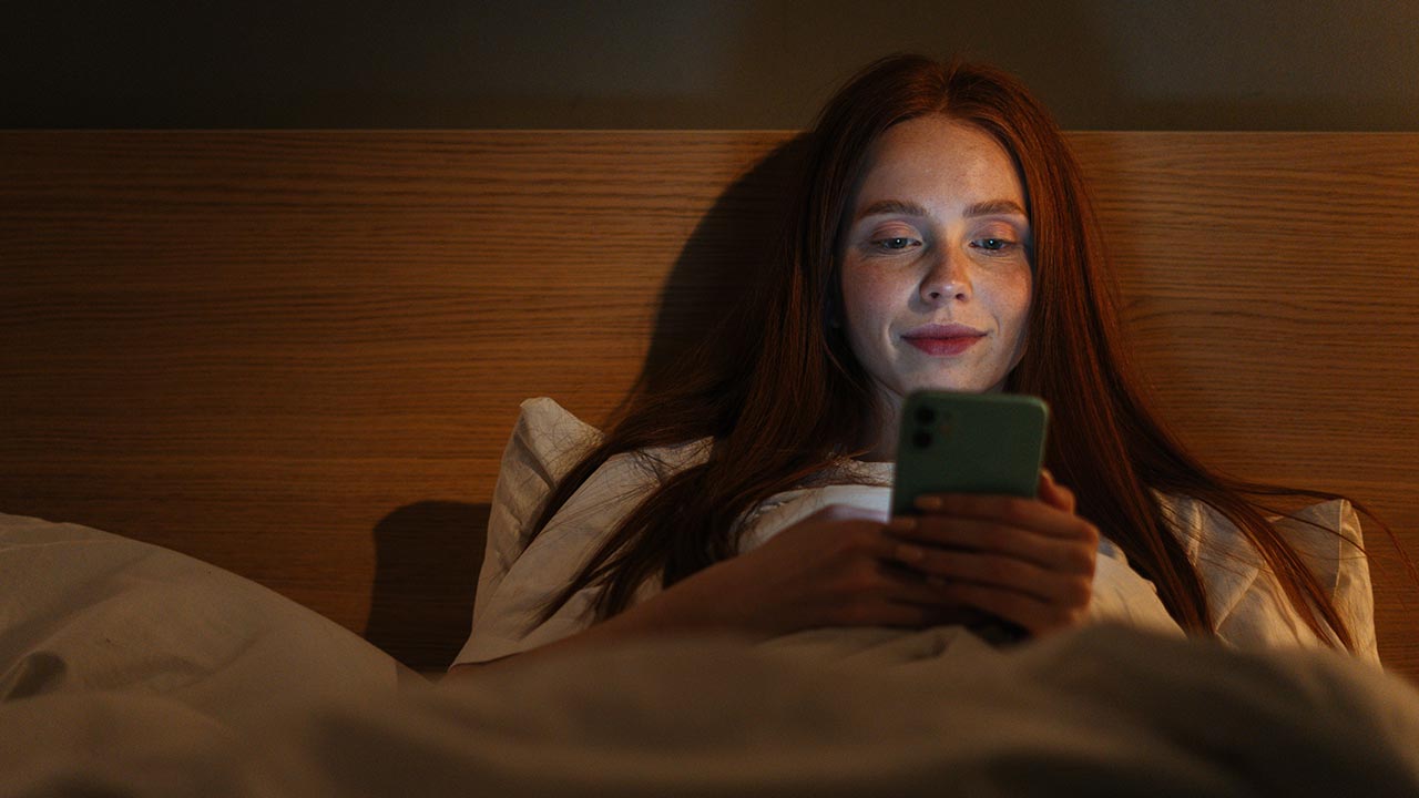 Mujer desplazándose por el teléfono en la cama.