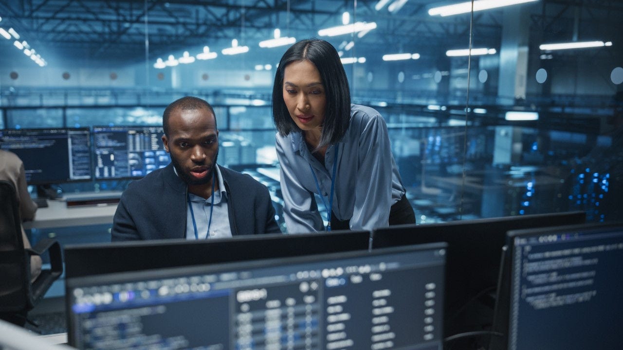 Two cybersecurity experts look at a monitor. 