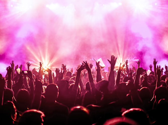 Une foule nombreuse et enthousiaste lors d’un concert, les mains levées vers les lumières de la scène, illustrant l’impulsion économique générée par les événements en direct.