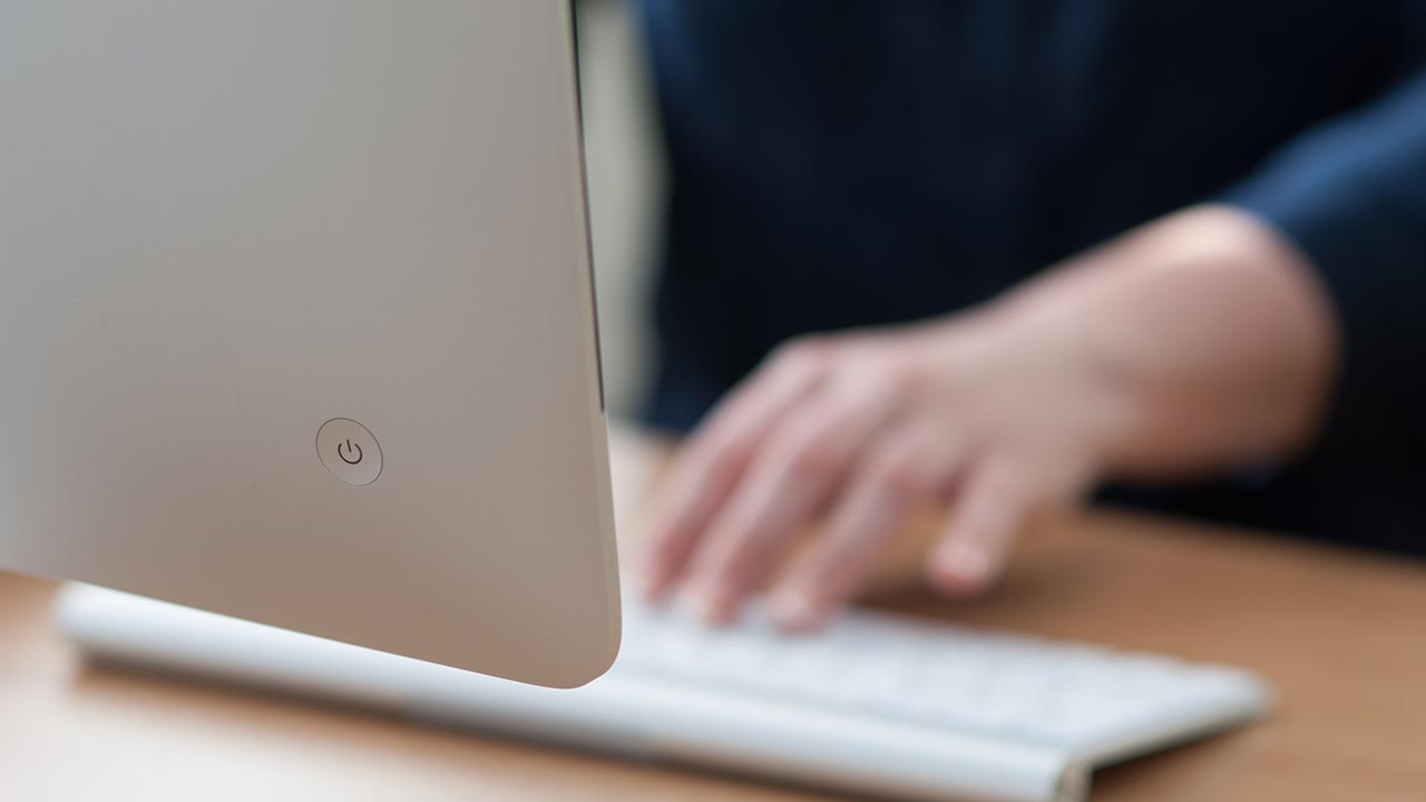 Computadora iMac vista desde atrás con una mano tocando el teclado.