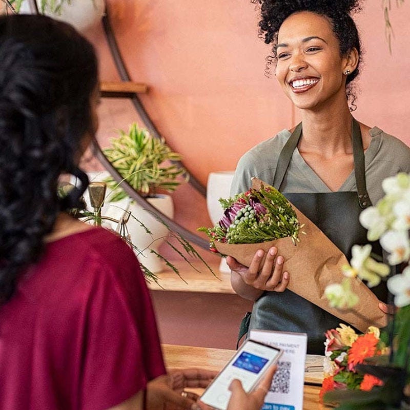 A florist holds a bouquet while a woman pays via mobile wallet. 