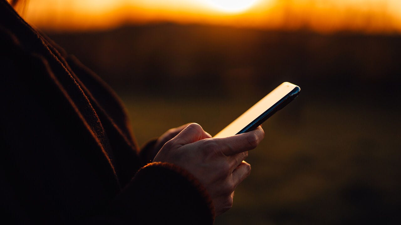 Una persona sostiene un teléfono al aire libre durante la puesta de sol.