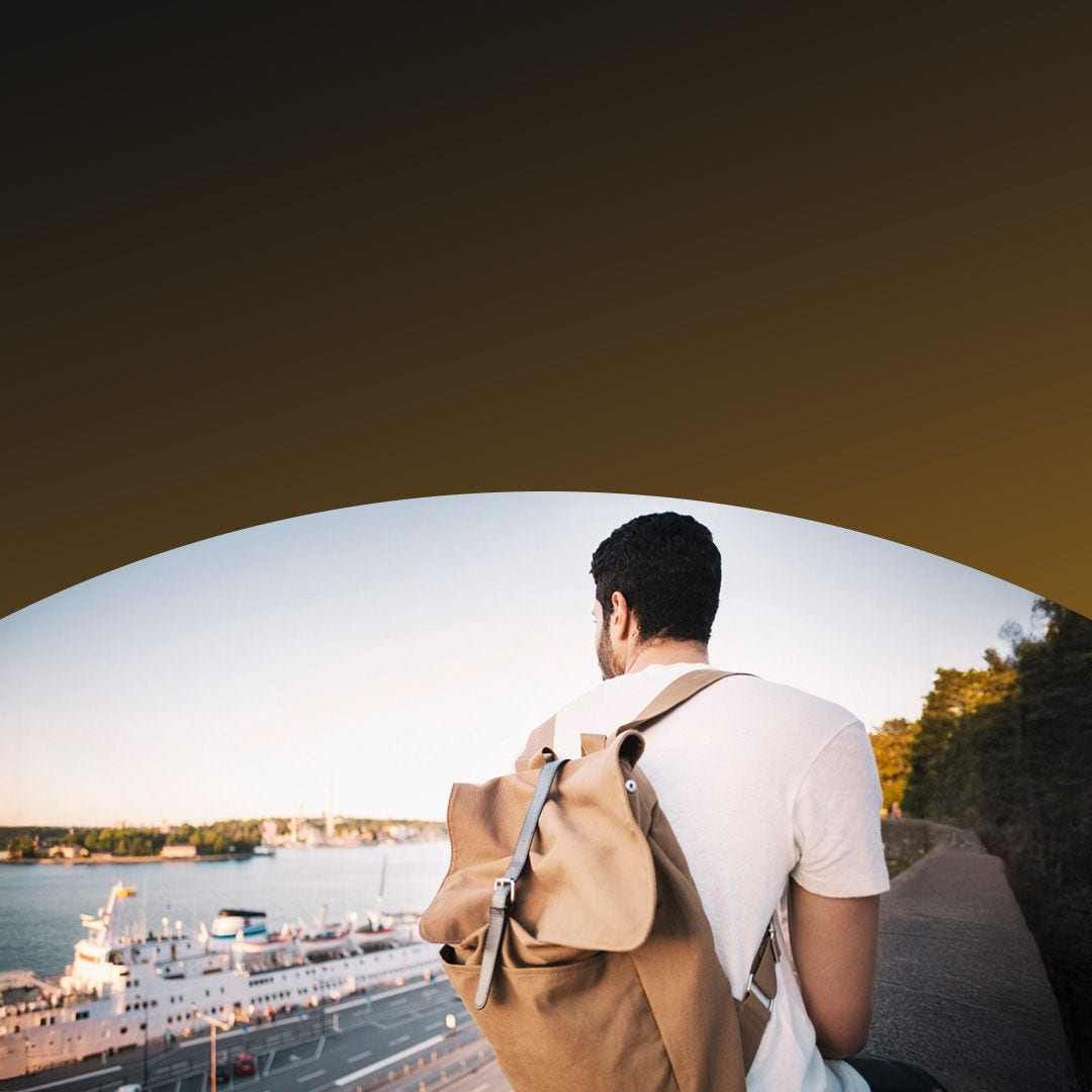 Male wearing backpack walking on sidewalk along waterfront.