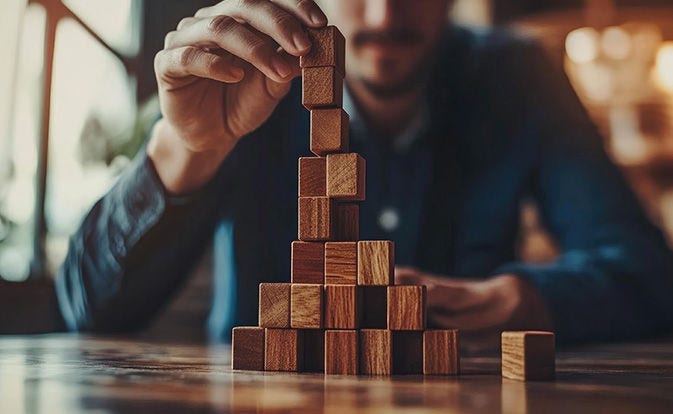 Mano colocando un bloque de madera sobre una torre que crece.