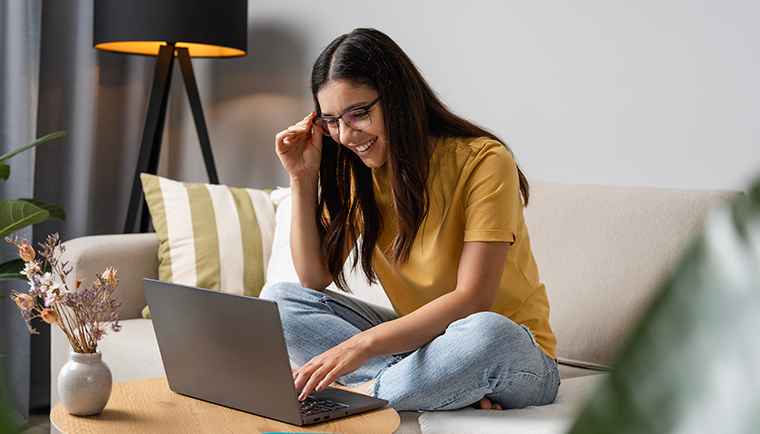 Woman smiling on couch looking at her laptop