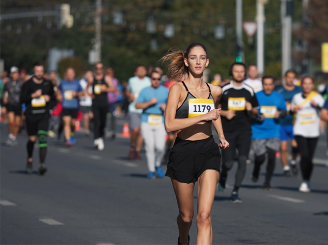 Une jeune femme courant pendant un marathon avec d'autres participants en arrière-plan.