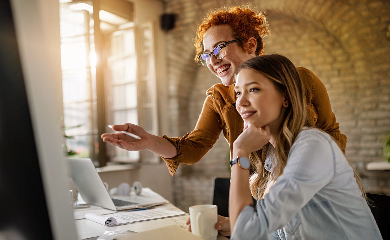 Dos mujeres sentadas en un escritorio, concentradas en una computadora, que participan en una discusión o colaboración.