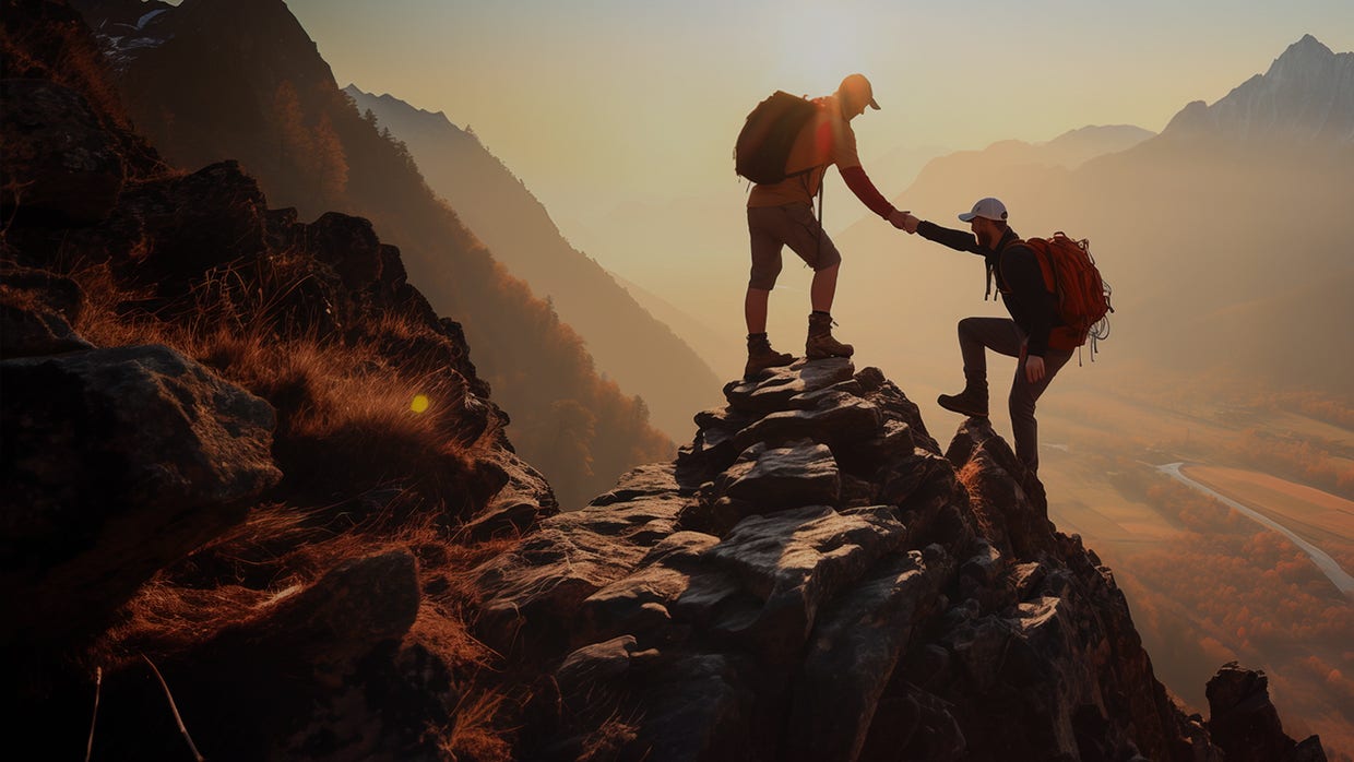 Deux randonneurs s'entraident au sommet d'une montagne. 
