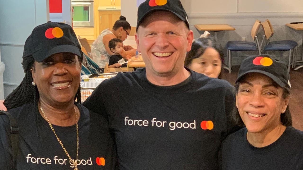 Três pessoas sorridentes usando camisetas e bonés com o logotipo da Mastercard.
