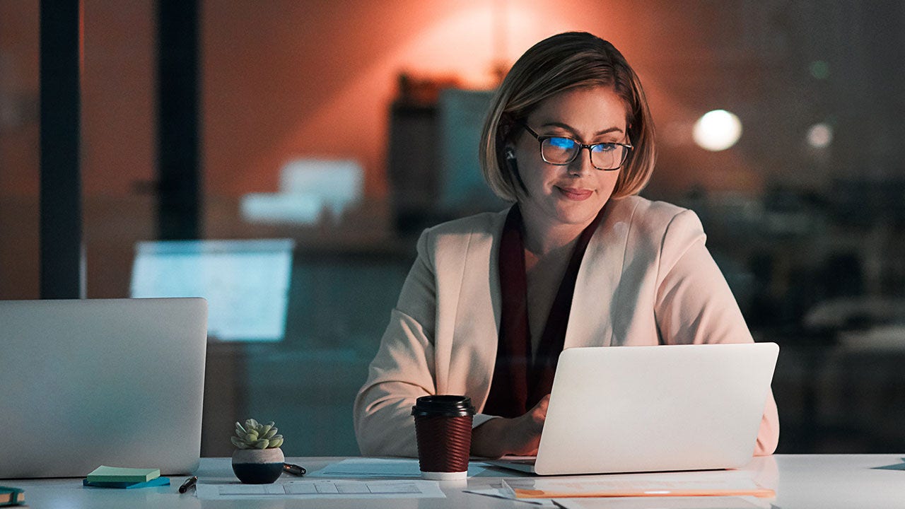 Una mujer de negocios usando una computadora portátil en su escritorio a altas horas de la noche en el trabajo.