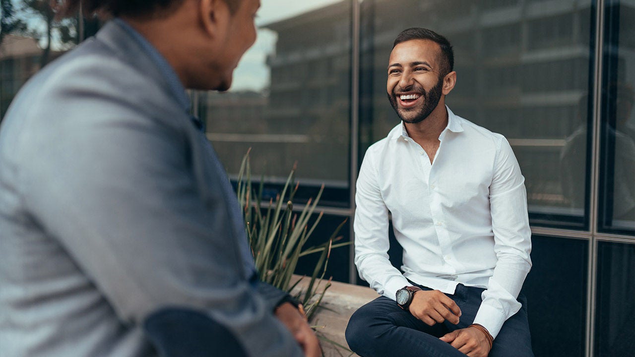 Two trendy businessmen talking and laughing casually outside.